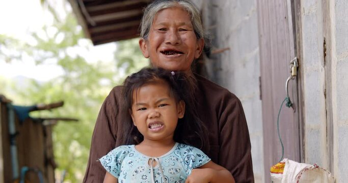 A smiling and laughing female Asian farmer which is an elderly poor farm worker, chewing betel nut and red lime, take care of granddaughter in a rural area.