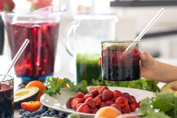 A glass of smoothie from berries in a child's hand at home in the kitchen.