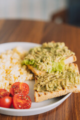 Healthy breakfast omelette with tomatoes and avocado toast on a white round plate.
