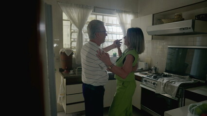 Romantic senior couple dancing in kitchen setting, retired older man and woman engaged in dance at home, authentic domestic lifestyle scene