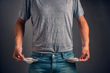 Man in gray crumpled T shirt and jeans with turned out, empty pockets.Concept of bankruptcy and...