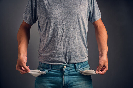 Man in gray crumpled T shirt and jeans with turned out, empty pockets.Concept of bankruptcy and poverty.