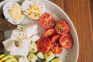 Vegetable salad with cheese and eggs and rye bread on a white plate.