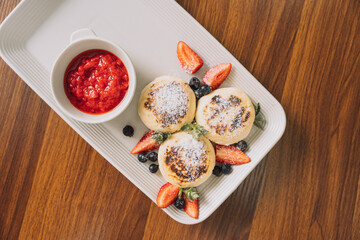 Cottage cheese pancakes with strawberries on rectangular plate with sauce on wooden table.