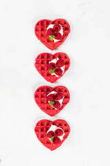 Red heart-shaped waffles with cream cheese, raspberries and micro greenery. White background. Top view