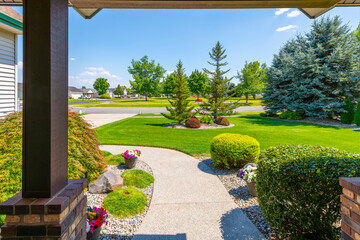 View from the front porch of a modern suburban home with a manicured front lawn in a nice community neighborhood across the street to a park on a sunny summer day. - obrazy, fototapety, plakaty