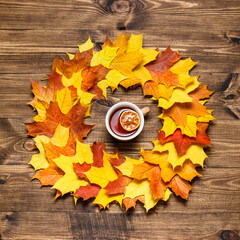 Autumn mood composition background. Cup of tea with round frame made of fallen autumn dried leaves on wooden table. Colorful, variegated foliage, warming drink. Flat lay, top view, copy space.