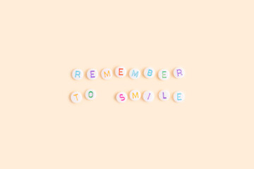 Remember to smile. Quote made of white round beads with multicolored letters on a beige background.