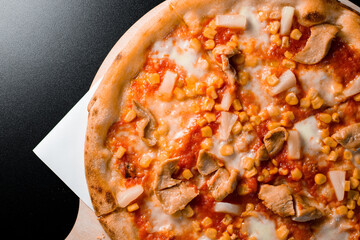 Tropical pizza with tomato sauce, mozzarella cheese, sweet corn, chicken and pineapple isolated over black background