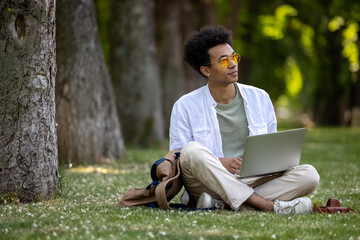 Obraz premium Young curly-haired man working on laptop in the park