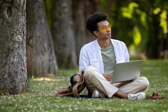 Young curly-haired man working on laptop in the park