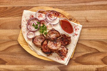 Fried veal meat with red onion rings, sauce and pita bread on the wooden board on the wooden table, flat lay top view