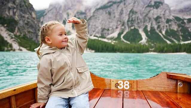 Little girl sitting in big brown boat at Lago di Braies lake in cloudy day, Italy. Summer vacation in Europe