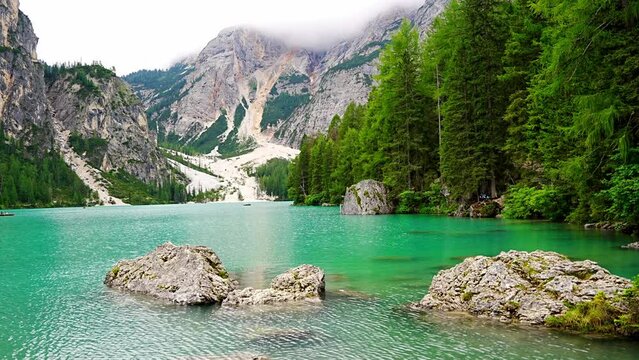 Braies lake surrounded by pine forests and the rocky ranges of the Dolomites in cloudy day, Italy.