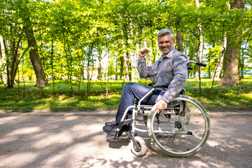 Gray haired disable man in wheelchair spending free time in park.