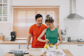 Husband looking at wife who cooking lunch for him. Happy asian couple in kitchen