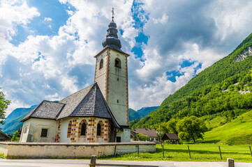 Fototapeta premium A view towards the church of Saint Paul in the alpine village of Stara Fuzina above lake Bohinj in Slovenia in summertime