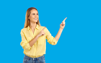 Smiling Caucasian young woman isolated on blue studio background point at good sale deal. Happy millennial girl recommend promotion or discount. Copy space, advertising placement.