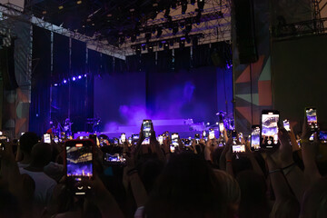 People in concert at music festival with hands with cell phones recording