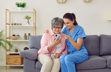 Young nurse helping a senior woman learn to use a mobile phone. Friendly caregiver showing a happy...