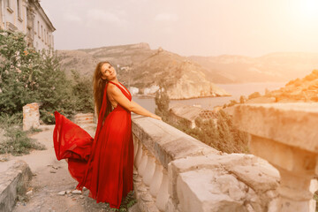 Woman red dress. Summer lifestyle of a happy woman posing near a fence with balusters over the sea.