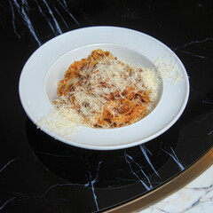 classic pasta spaghetti bolognese with a hat of parmesan on a black marble table