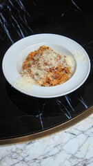 classic pasta spaghetti bolognese with a hat of parmesan on a black marble table