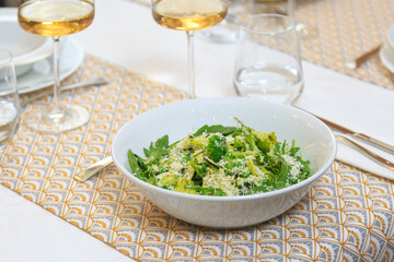 green salad in a deep white salad bowl served with a knife and fork with a glass of water and wine