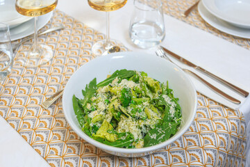 green salad in a deep white salad bowl served with a knife and fork with a glass of water and wine