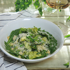 green salad in a deep white salad bowl served with a glass of wine on a rustic wooden table on a napkin