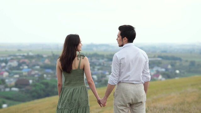 Young couple lovingly looks at each other kissing on hill against village houses downward. Concept of love and view from hilly plain slow motion
