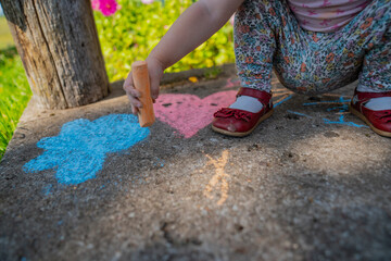 Child toddler girl with small red shoes drawing with chalk on countryside porch during summer evening