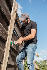 Fototapeta premium Man work on holiday repairing and renovating a country house - summer chores in the backyard and garden - power tool work