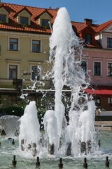 Aphrodite fountain spurting water against the background of tenement houses in the Old Market Square in Płock.