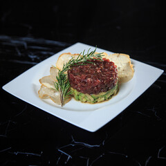 tuna tartar on a bed of chopped avocado and bread chips on a black marble table