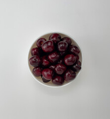 Cherry berries in a white bowl isolated on a white background, top view, copy space.