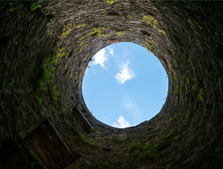 Stone well hole, old construction from inside, brick walls and blue sky background, fall down in...