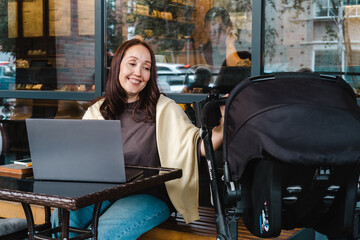 Middle aged mother working in cafe outside whith her child in baby carriage