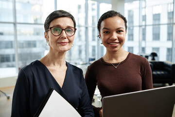 Front view portrait of two modern businesswomen smiling at camera in luxury office interior