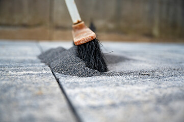 Broom pushing a tile gaps sand in between concrete tiles for outdoor patio