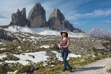 A woman with trekking poles stands in front of Tre Cime di Lavaredo