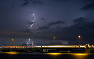 Sky during a bad storm with thunder and lightning over the sea. Shot of a bridge with cars passing...