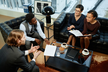 High angle portrait of group of successful business people meeting over coffee table in luxury...