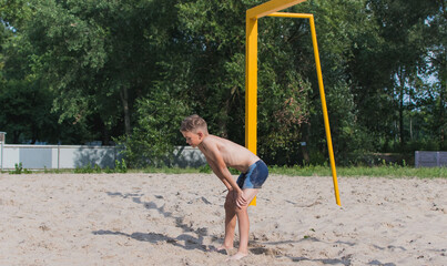 A little boy is playing soccer on the sand