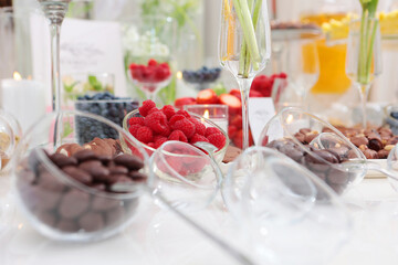 Raspberries and sweets on table.Party with light snacks.Glassware is out of focus.
