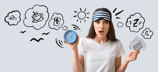 Troubled woman with sleeping pills and clock on light background