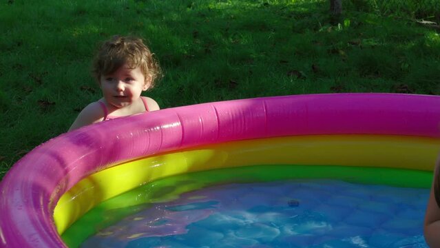 Children in the pool, it's hot in the summer. A little girl. A child plays in a children's pool. Swimming in the yard, inflatable pool in the shade. The girl loves water. Happy child in a swimsuit