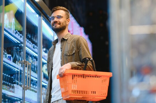 Man with a beard buys a beer in the alcohol department of a supermarket . Handsome man chooses a beer bottle in the store and communicates on a smartphone.Shopping in a supermarket
