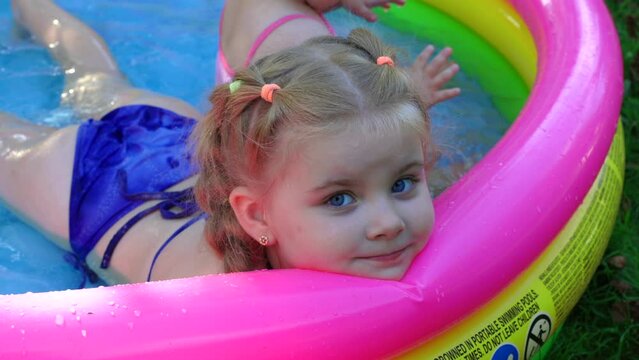 Children in the pool, it's hot in the summer. A little girl. A child plays in a children's pool. Swimming in the yard, inflatable pool in the shade. The girl loves water. Happy child in a swimsuit