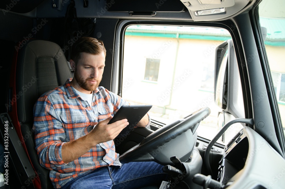 Wall mural man truck driver sitting behind wheel of car and holding digital tablet in his hands